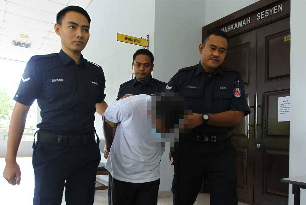 Tertuduh (berbaju putih) diiring polis ketika hadir ke mahkamah.