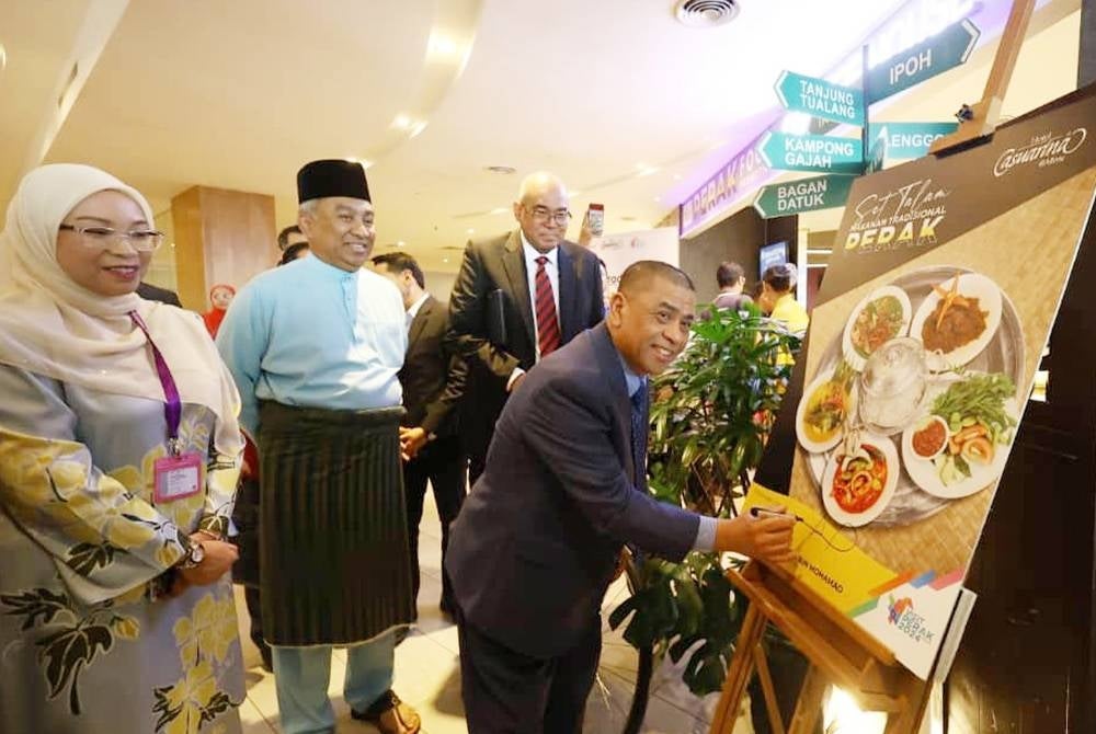 Saarani menandatangani plak simbolik melancarkan promosi Makanan Tradisi Perak sambil diperhatikan Sabrina (kiri) di Hotel Casuarina@Meru pada Jumaat.