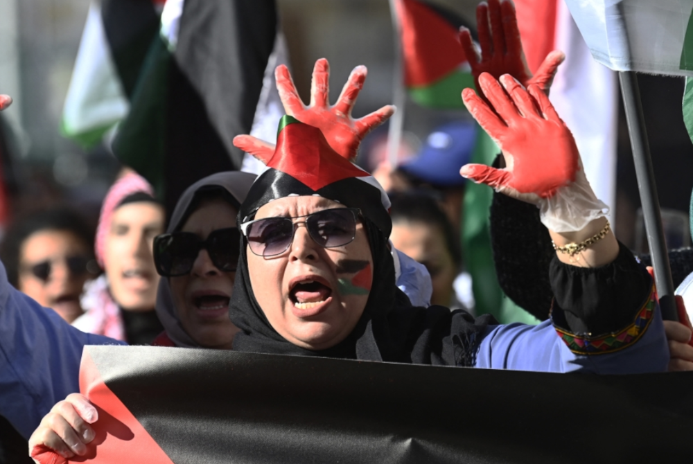 Orang ramai menunjukkan tangan mereka dicat merah semasa tunjuk perasaan menyokong rakyat Palestin di Valencia pada Ahad. - Foto JOSE JORDAN/AFP