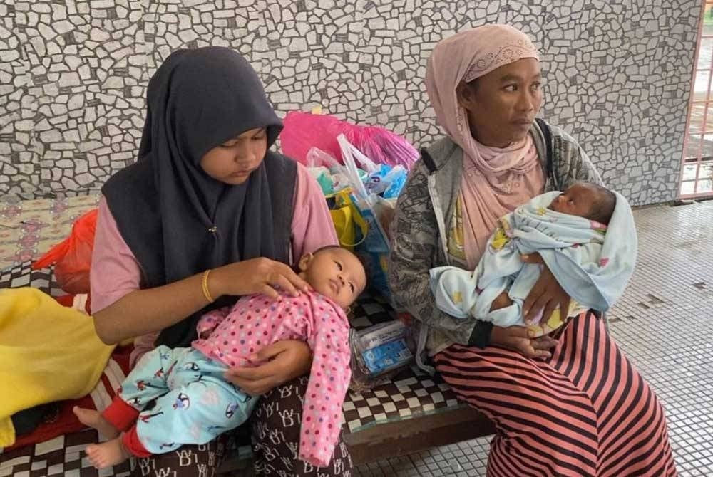 Maisanah (kanan) dari Kampung Dalam Rhu, Pasir Puteh terpaksa meredah banjir sedalam 0.4 meter bersama bayinya selepas rumah ditenggelami air sejak malam Isnin.