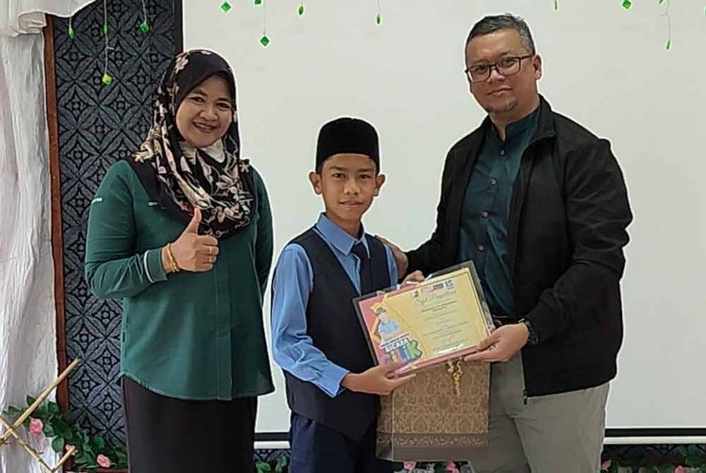 Dr Mohamad Riza (kanan) diiringi Izzan Haslinda menyampaikan menyampaikan hadiah kepada Ahmad Muaz yang terpilih antara pembentang terbaik Bicara Cilik Rasuah Busters Peringkat Kebangsaan 2023 kategori sekolah rendah dalam majlis penyampaian hadiah di SK Tanah Puteh, Pekan pada Rabu.