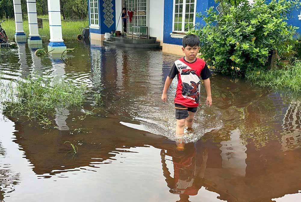 Seorang kanak-kanak mengharungi air yang bertakung di hadapan rumah keluarganya.