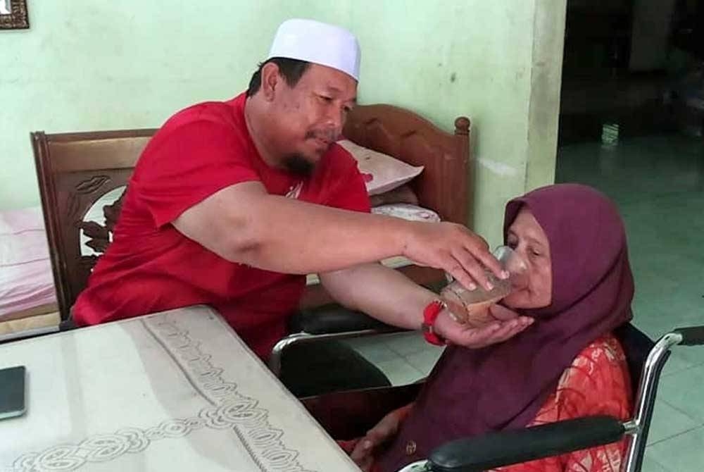 Afandi memberi minum kepada ibu mentuanya, Rafeah di kediaman mereka di Felda Bukit Goh di sini pada Selasa.