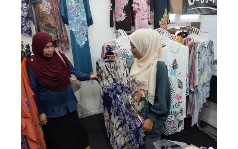 Ros Aiza (kanan) sedang melayan seorang pelanggan yang ingin membeli baju yang dihasilkannya.