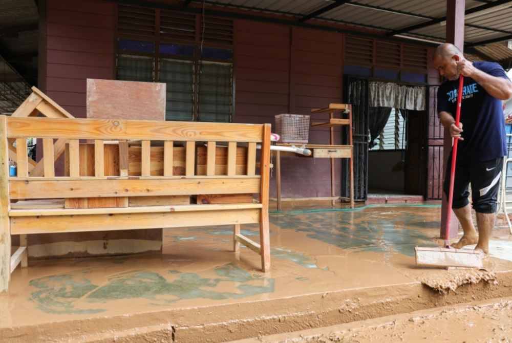 Murad membersihkan kediamannya yang dinaiki air sehingga lebih satu meter di Kampung Paya Kenangan. - Foto Bernama