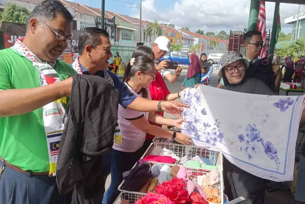Mas Imran (kiri) dan Fauzi (tengah) melawat booth jualan dalam Program Jualan Amal Gaza di tapak parkir Pasar Raya Econsave Taman Teratai, Johor Bahru pada Sabtu.