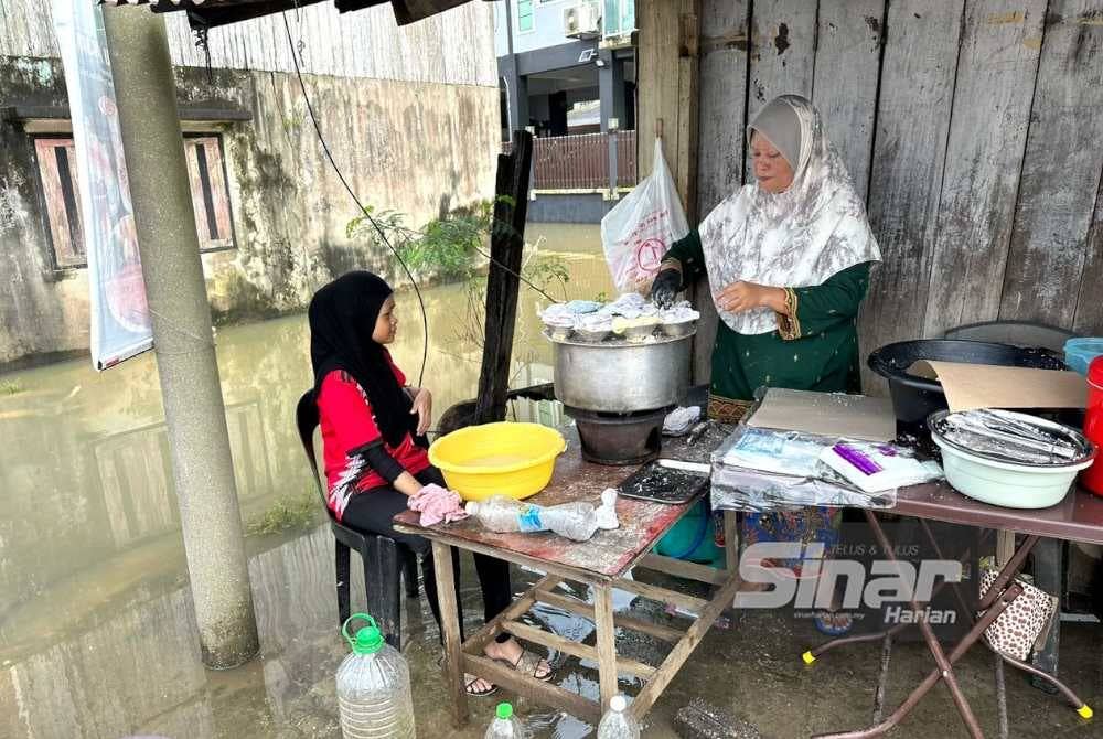 Azizah (kanan) dibantu Siti Nur Hafifi (kiri) berniaga putu halba walaupun kawasan di sekitar gerainya dinaiki air.