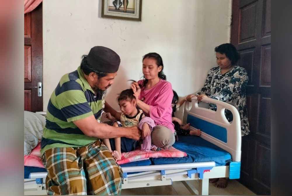 Mohd Zaidi (kiri) membantu isterinya menguruskan Muhammad Qhalis Qashah di rumah mereka di Simpang Semabok.