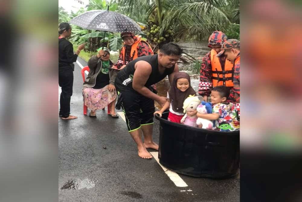 Anggota bomba membantu memindahkan kanak-kanak yang terperangkap akibat banjir di Kampung Parit Abas, Benut pada petang Rabu. - Foto bomba