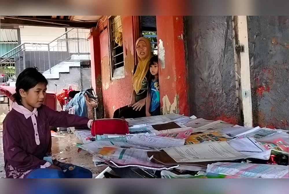 Norlizah (duduk) melihat anaknya mengemas buku selah yang rosak susulan banjir.