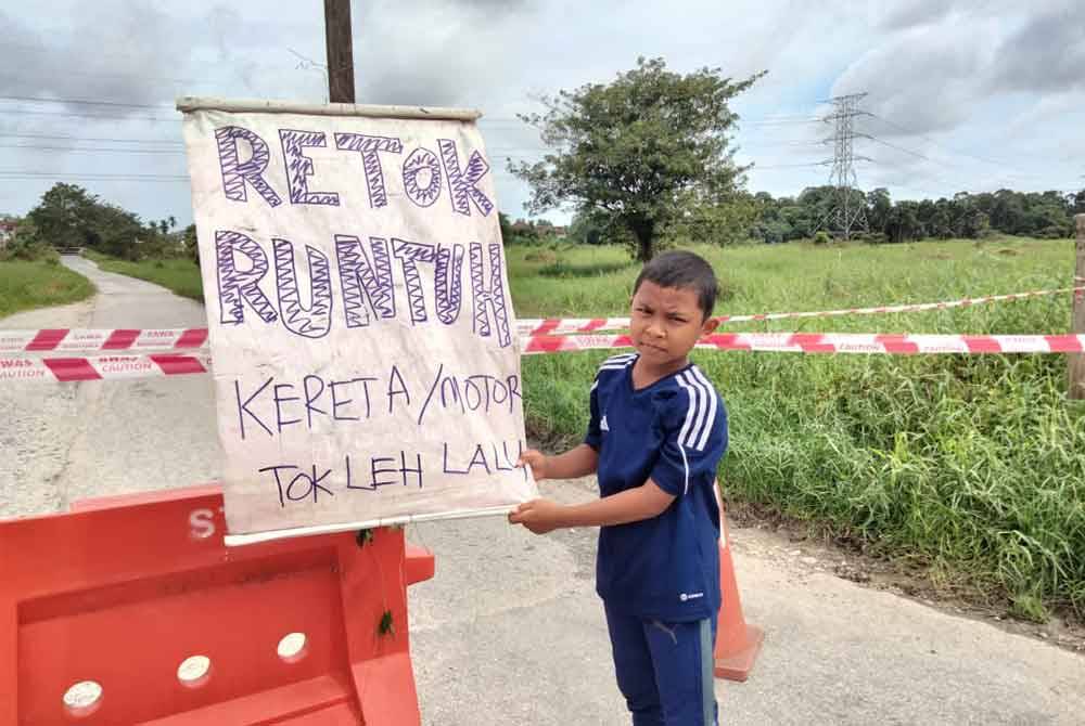 Muhd Iqbal Yusran, 10, memegang tanda amaran runtuhan tebing jambatan di Kampung Jelatang