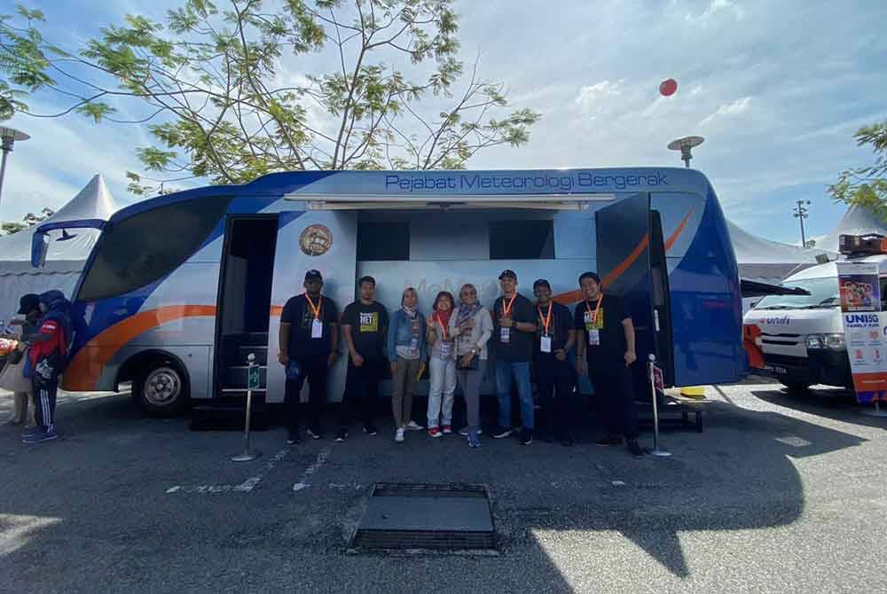 Pegawai MetMalaysia bergambar di sebelah Pejabat Meteorologi Bergerak di pekarangan Stadium Nasional Bukit Jalil.