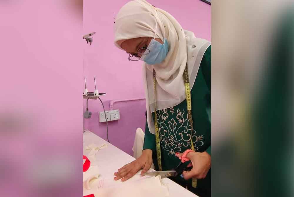 Irfa memotong kain untuk menjahit tempahan pelanggan.