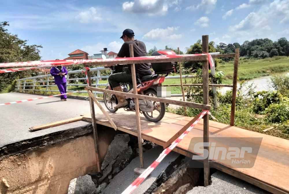 Wan Mohd Zulfahmi melalui jambatan sementara yang dibina sekumpulan penduduk.