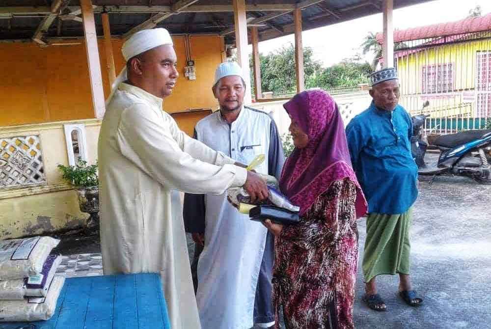 Sabri ( kiri) menyerahkan beras cupak kepada penduduk.