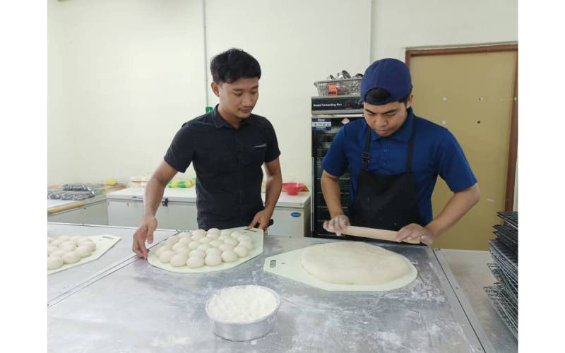 Muhamad Syirazi (kiri) melihat pekerjanya menguli tepung untuk pembuatan roti burger.
