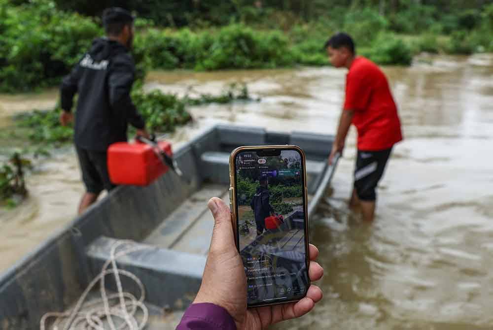 Penduduk Kampung Manal, Mohamad Yufaizal Mohd Yusoff menggunakan aplikasi Tik Tok untuk mengemas kini situasi banjir di penempatan itu kepada warga maya ketika tinjauan sekitar Kampung Manal hari ini. - Foto Bernama