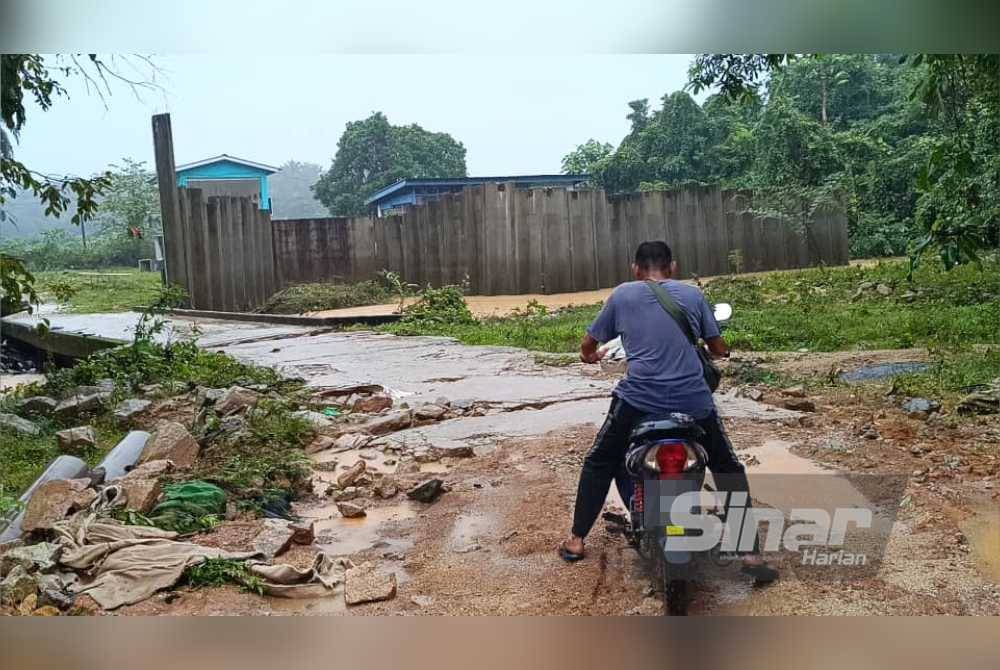 Motosikal ditunggang seorang penduduk melalui jalan rosak untuk menyeberang jambatan
