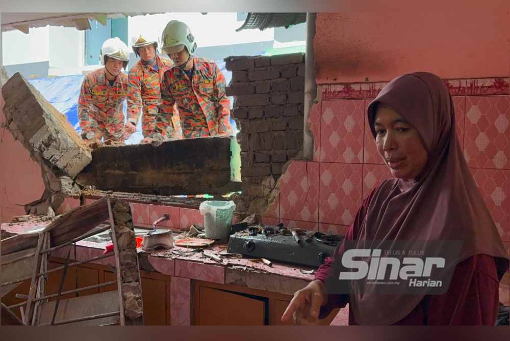 Nor Silawati (kanan) melihat dinding dapur rumah yang runtuh.