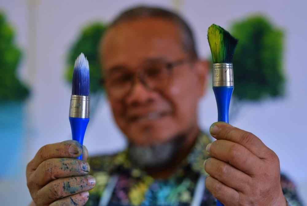 Ismail Ahmad menunjukkan jenis berus yang digunakan untuk menghasilkan karya seni..