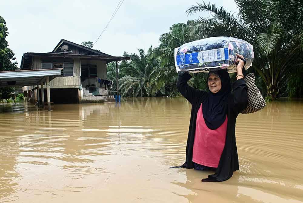 Robiah Salim, 65, meredah banjir untuk ke PPS dengan membawa barang keperluan selepas pulang melihat keadaan rumahnya ketika tinjauan di Kampung Pengkalan Ajal. - Foto Bernama