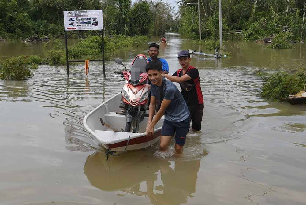 Mohamad Izzat (belakang) bersama dua rakannya membantu memindahkan motosikal penduduk dari Kampung Serongga ke lokasi lebih tinggi susulan paras air Sungai Teresek semakin meningkat sejak petang semalam. - Foto Bernama