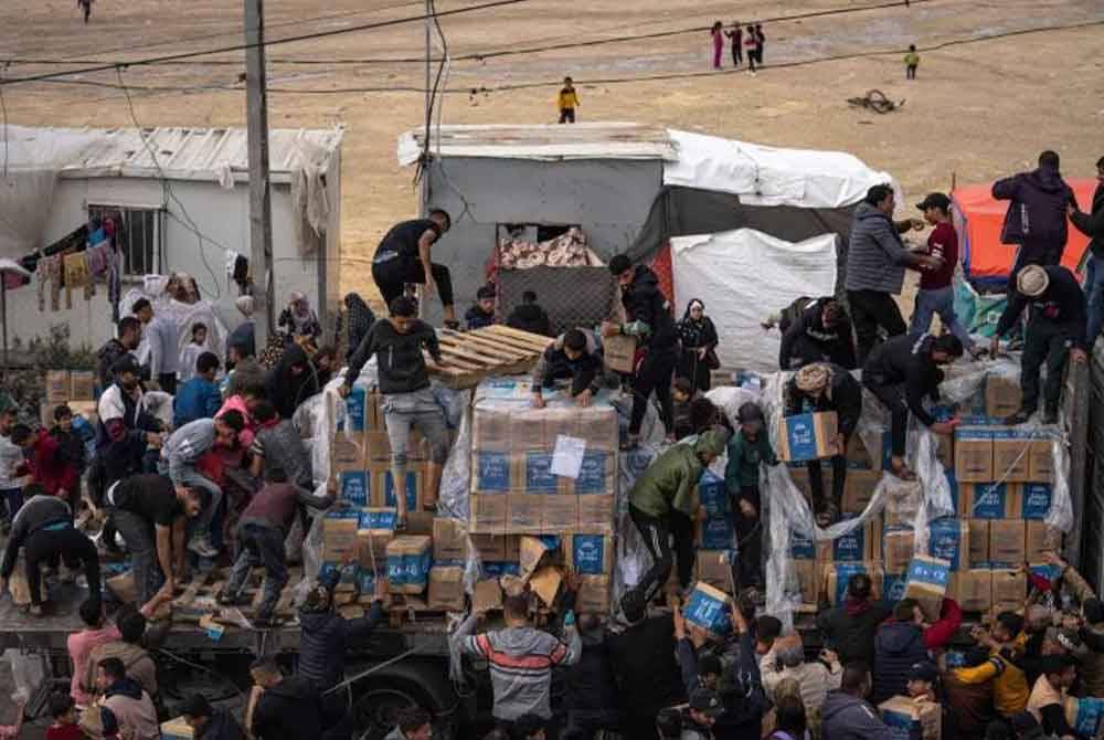 Puluhan yang terdesak memanjat trak dan mengagihkan sendiri kotak bantuan kepada saudara mereka yang lain. - Foto Agensi
