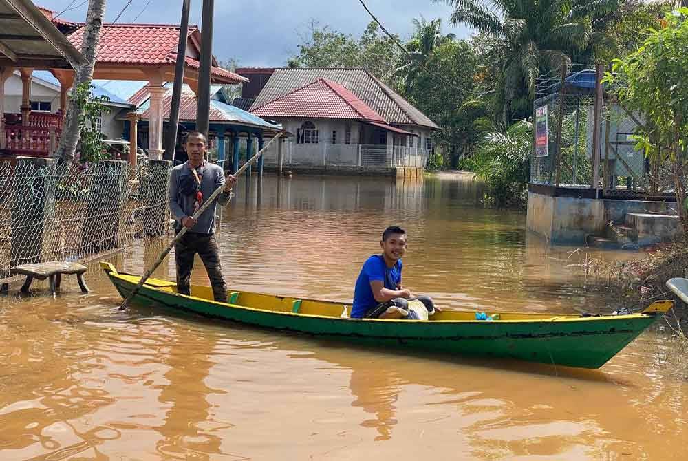 Mohd Ahdi Ahlam (kanan) terpaksa berulang alik tiga kali sehari menaiki perahu untuk memeriksa keadaan rumah di Kampung Kusar, Rantau Panjang.