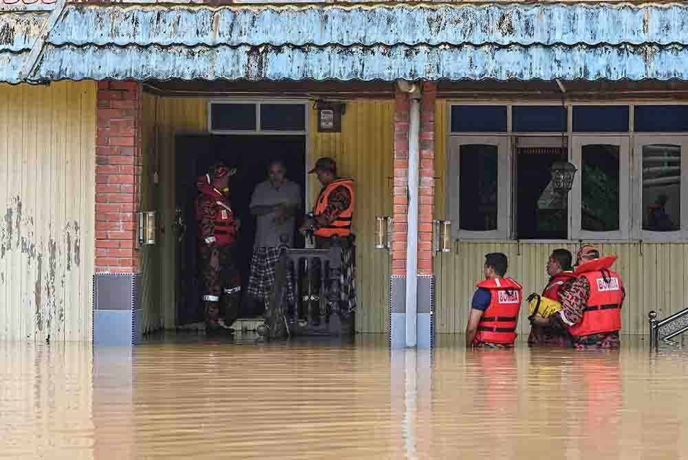 Hassan (kiri) bersama pegawai memujuk seorang penduduk yang masih tinggal dirumahnya selepas kawasan berkenaan dinaiki air semasa membuat pemantauan di Kampung Bukit Tok Bat hari ini. Foto Bernama