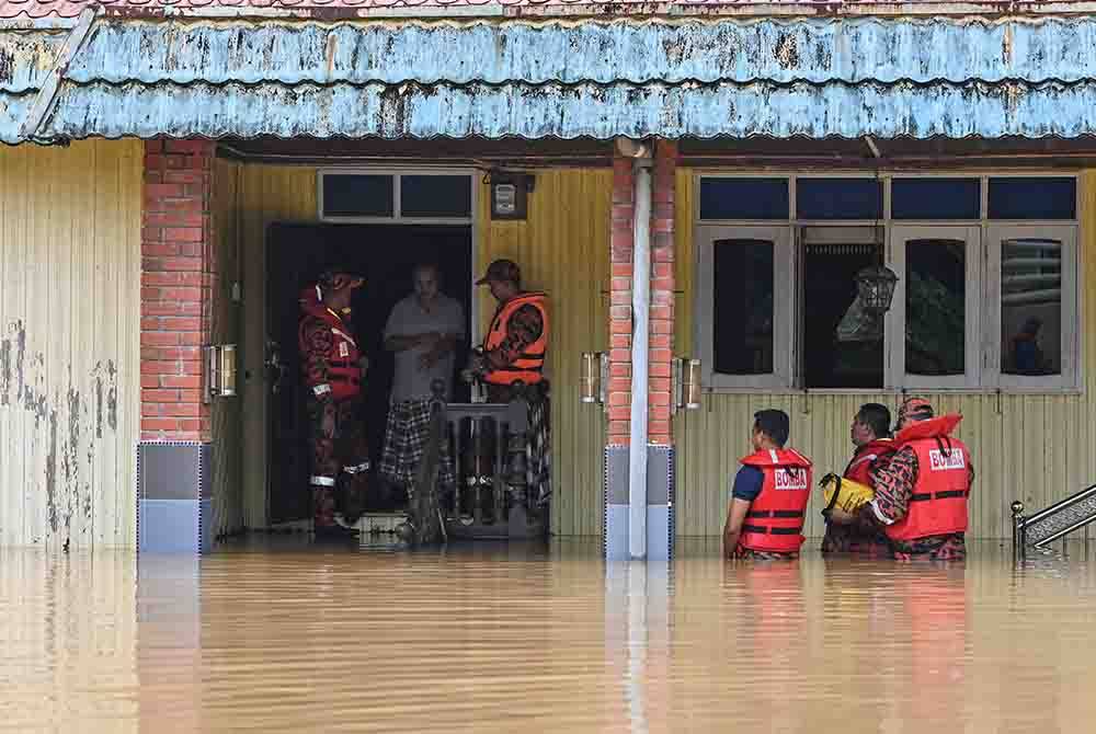 Pengarah JBPM Terengganu, Hassan 'As'ari Omar (kiri) bersama pegawai memujuk seorang penduduk yang masih tinggal dirumahnya selepas kawasan berkenaan dinaiki air semasa membuat pemantauan di Kampung Bukit Tok Bat pada Selasa. - Foto: Bernama