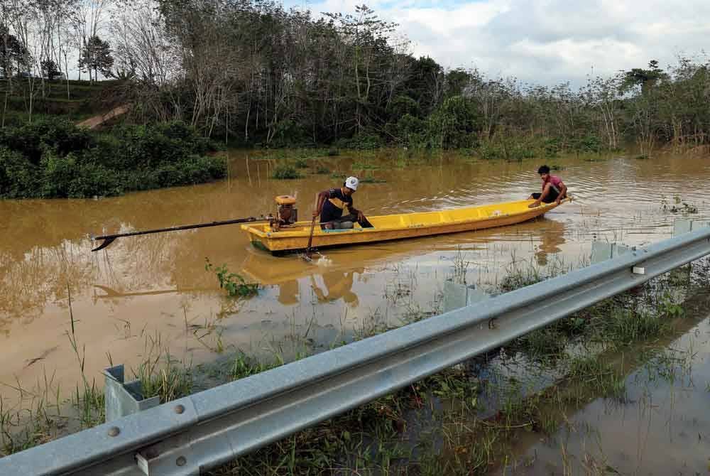 Penduduk kampung yang terputus hubungan terpaksa menggunakan sampan untuk menyeberangi air banjir di Jalan Kampung Pemberian susulan limpahan air Sungai Lebir. - Foto Bernama
