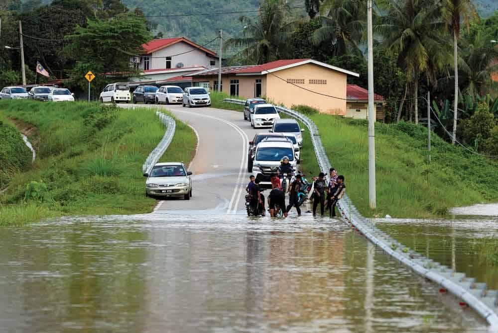 Penduduk kampung yang terputus hubungan disebabkan air banjir yang memenuhi Jalan Kampung Pemberian susulan limpahan air Sungai Lebir. - Foto Bernama
