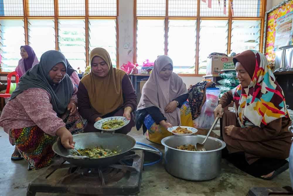 Zuraida (dua dari kanan) bergotong-royong bersama yang lain menyediakan makanan tengah hari di PPS Sekolah Menengah Kebangsaan Menerong, Ajil. - Foto Bernama