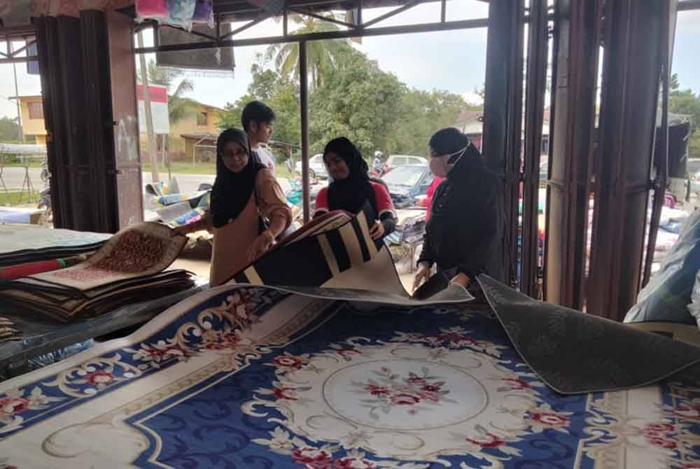 Noriah (kanan) memilih karpet yang dijual di sebuah kedai karpet di Jalan Pasir Mas-Rantau Panjang.