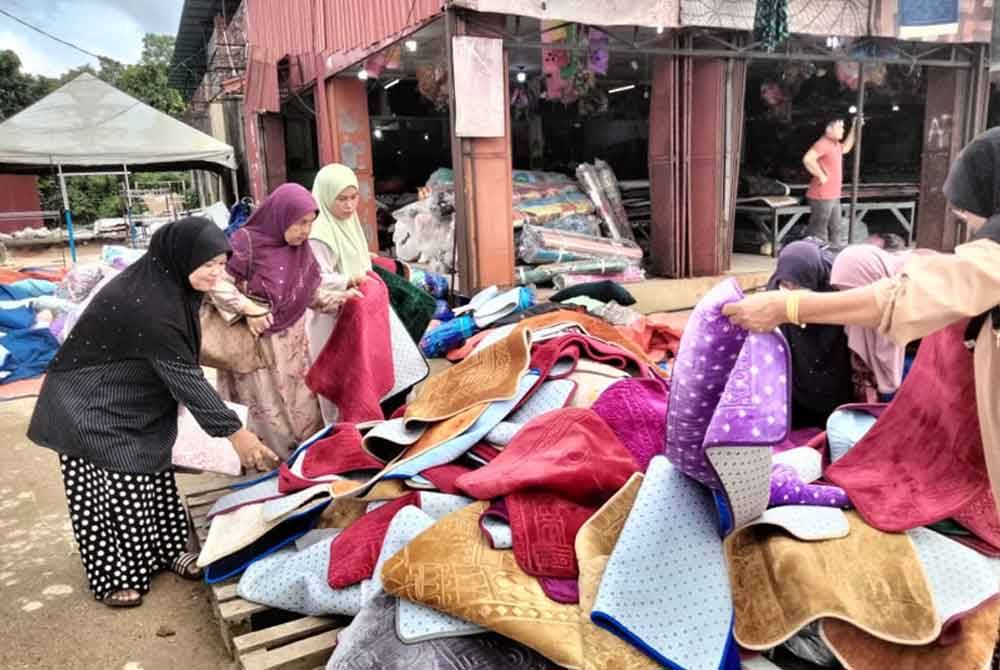 Nik Zuraini (kiri) memilih alas kaki yang dilelong di sebuah kedai karpet di Jalan Pasir Mas-Rantau Panjang.