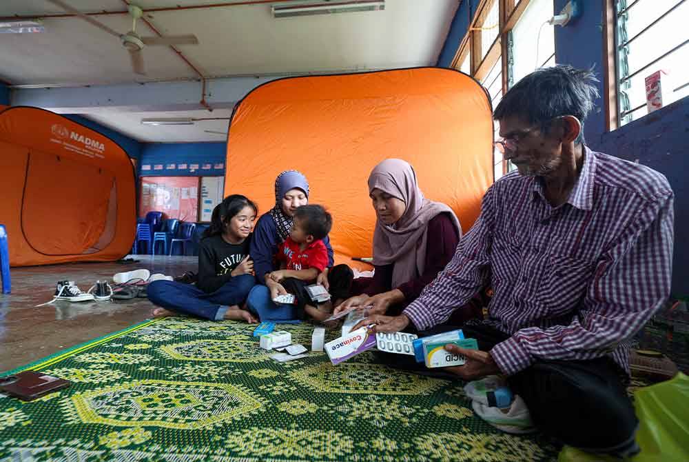Mangsa banjir, Adnan Daud, 54, bersama ahli keluarganya melihat ubat-ubatan yang dibawanya bersama ketika dipindahkan ke PPS Sekolah Kebangsaan Pemberian susulan limpahan air Sungai Lebir. - Foto Bernama