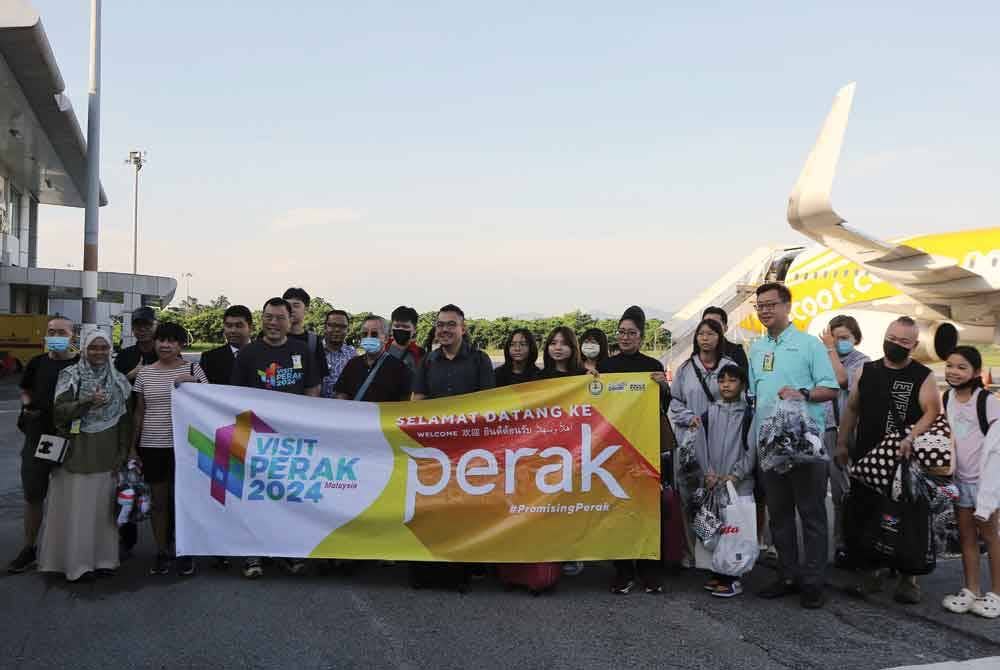 Sze Yee (tiga dari kiri) bergambar kenangan bersama pelancong dari Singapura yang selamat tiba pada jam 8.20 pagi di Lapangan Terbang Sultan Azlan Shah, pada Isnin. - Foto: Bernama