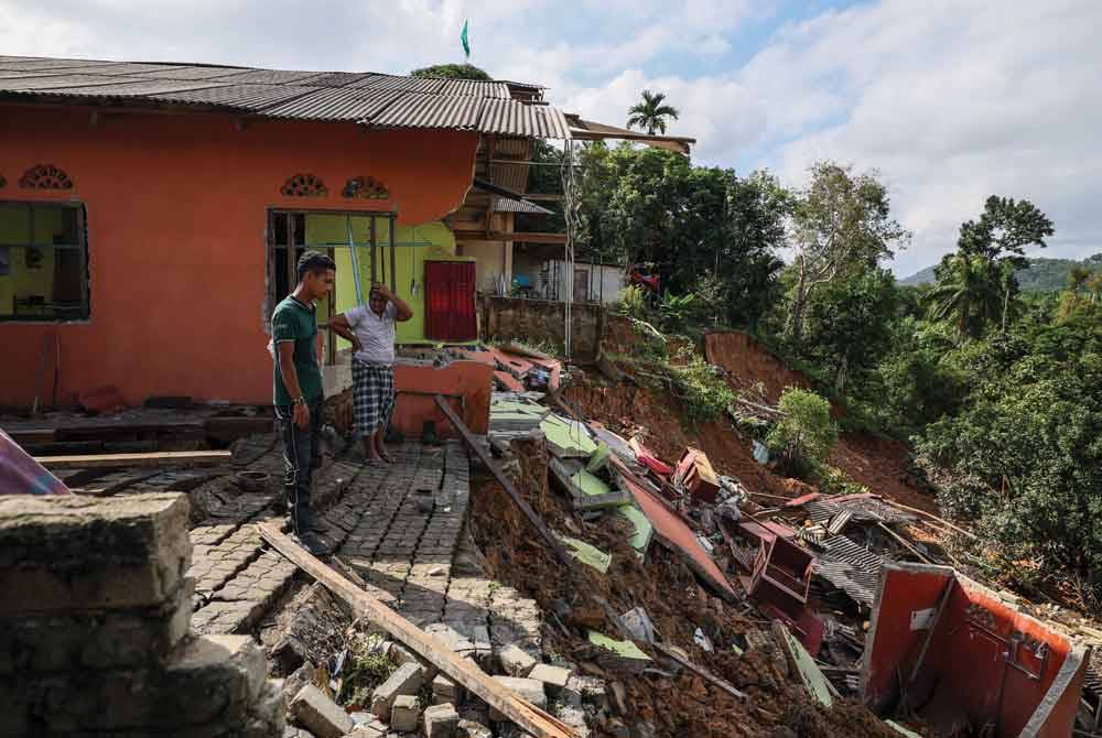 Muhammad Ubaidillah (kiri) bersama sepupunya Mohd Saiful Bahari Ismail, 31, meninjau kerosakan rumah akibat tanah runtuh di Felda Neram 2, Kemaman, pada Isnin. - Foto Bernama