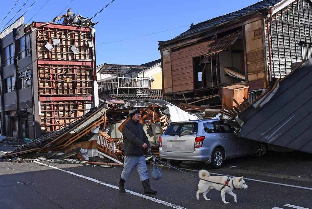 Seorang lelaki berjalan dengan seekor anjing lepasi bangunan musnah di Anamizu, wilayah Ishikawa pada Khamis, selepas gempa bumi 7.5 magnitud landa wilayah Noto di wilayah Ishikawa pada hari Tahun Baharu. Foto AFP