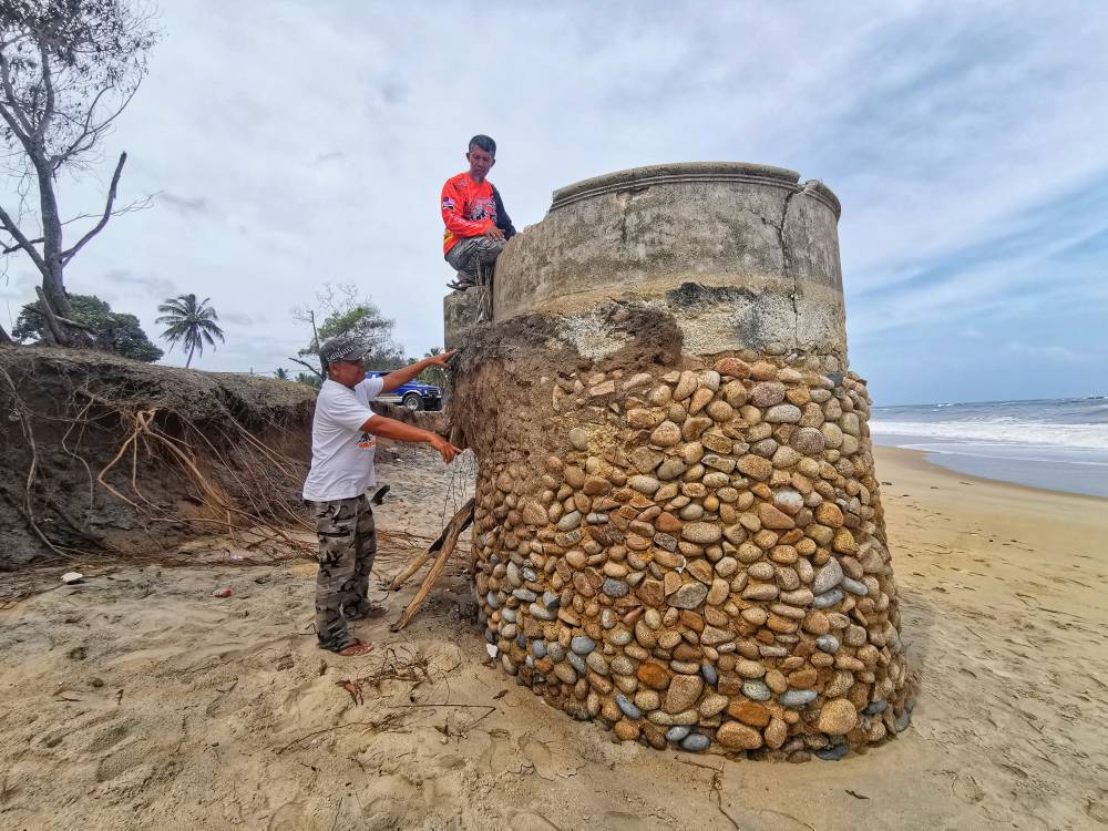 Anuar (kiri) bersama rakannya melihat keadaan perigi lama yang semakin timbul akibat masalah hakisan yang berlaku di kawasan itu.