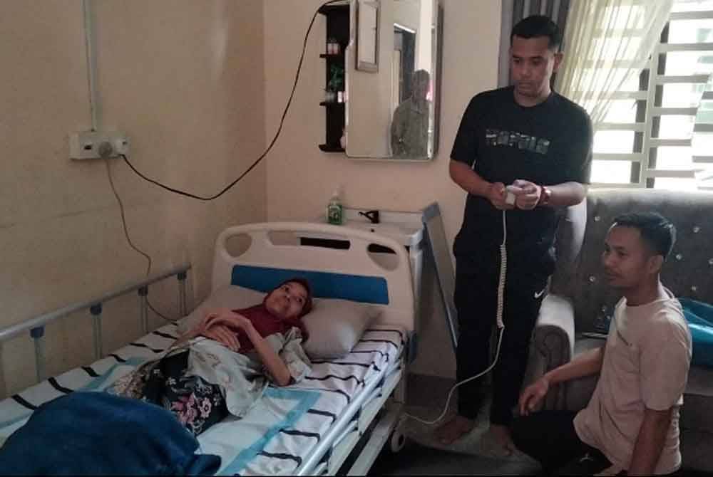 Idhan (tengah) menggunakan alat kawalan untuk melaras kedudukan katil elektrik Fatihah.