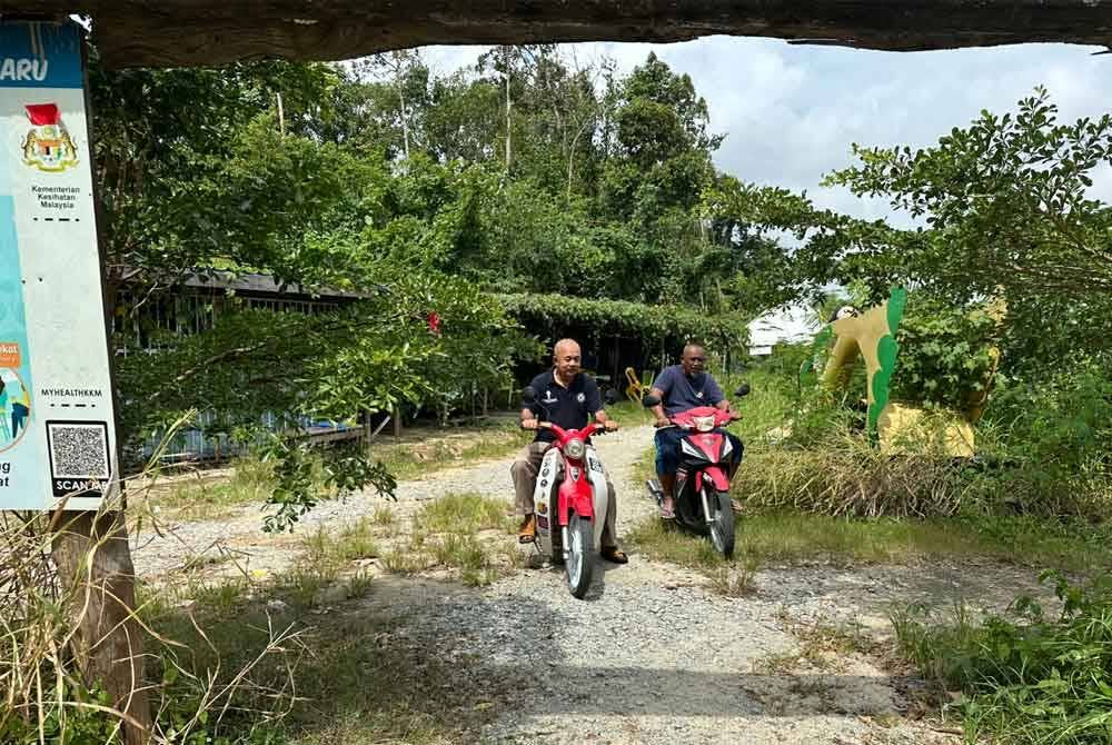 Johari (kiri) dan Rejuhan (kanan) menaiki motosikal di laluan masuk ke titi Kampung Pulau Tengah yang ditumbuhi semak-samun.