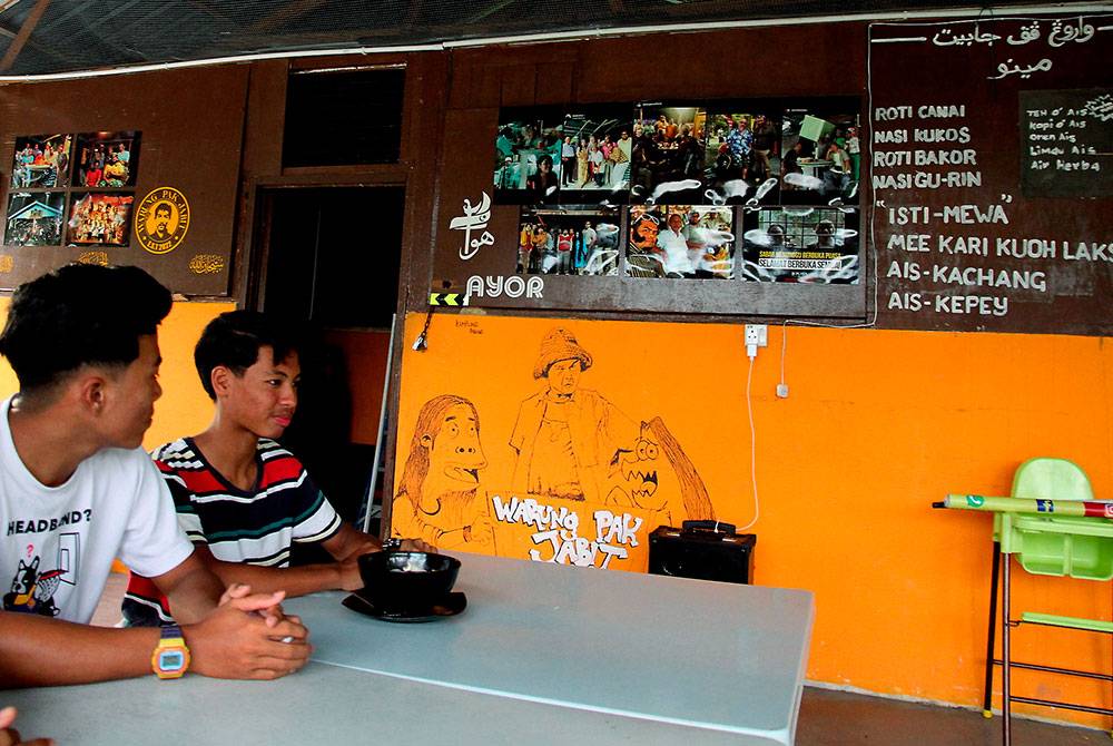 Pengunjung Putera Alhafiz Meor Aswad (kanan) menikmati hidangan menu Mee Kari Kuah Laksa bersama rakan di Warung Pak Jabit. Foto Bernama