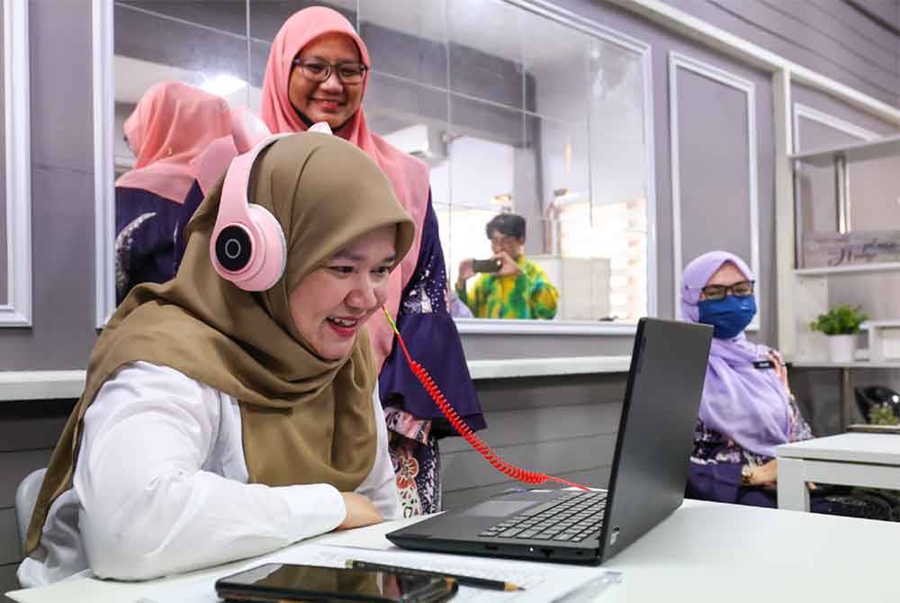 Fadhlina (duduk, kiri) berbual dengan pelajar sekolah menerusi PdPR ketika melakukan lawatan kerja berikutan gangguan bekalan air di SMK Seri Nibong. Foto Bernama