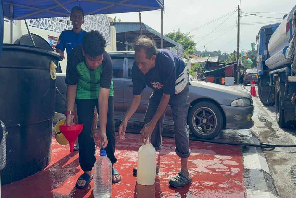 Petugas Masjid Ridwaniah sedang membantu penduduk sekitar Sungai Batu mengisi air daripada tangki fleksi ke dalam tong kecil dan baldi.
