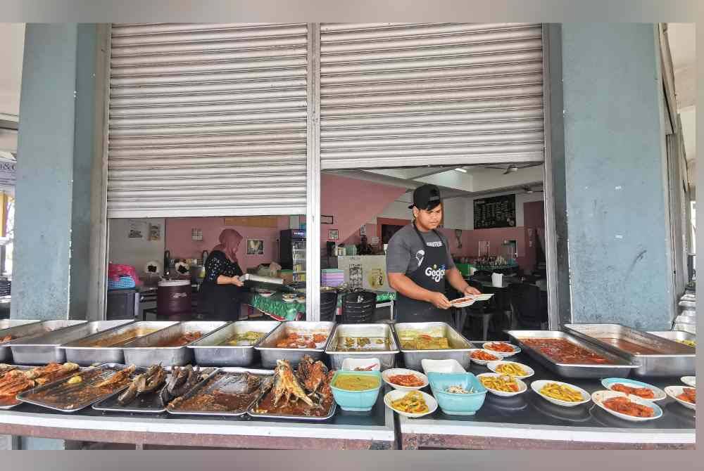 Sulaiman (kanan) menyusun lauk pauk sebelum menutup sementara operasi perniagaan selama dua jam pada Jumaat.