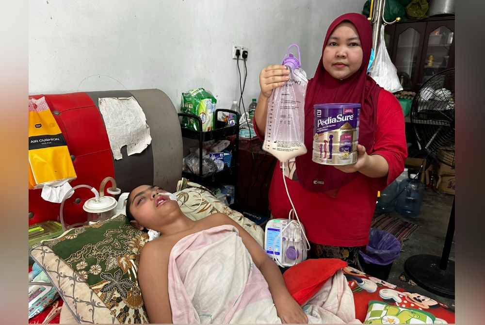 Siti Noor Mastubaidura (kanan) menunjukkan susu formula yang diperlukan Muhammad Aiman.