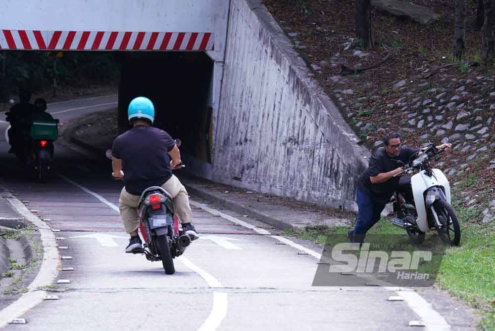 Seorang lelaki sedang mengalihkan motosikal yang terlibat dalam kemalangan di laluan khas motosikal.