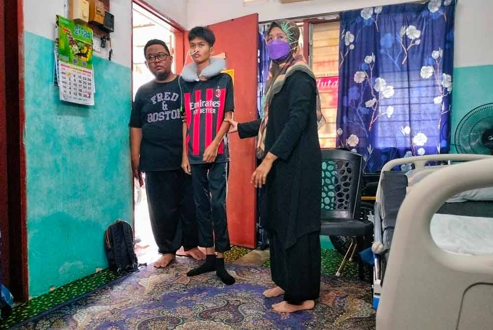 Irmi Shahrizan (kiri) memimpin anaknya yang tidak mampu berdiri sendiri di rumah mereka di Taman Bukit Rambai, di sini, pada Sabtu.