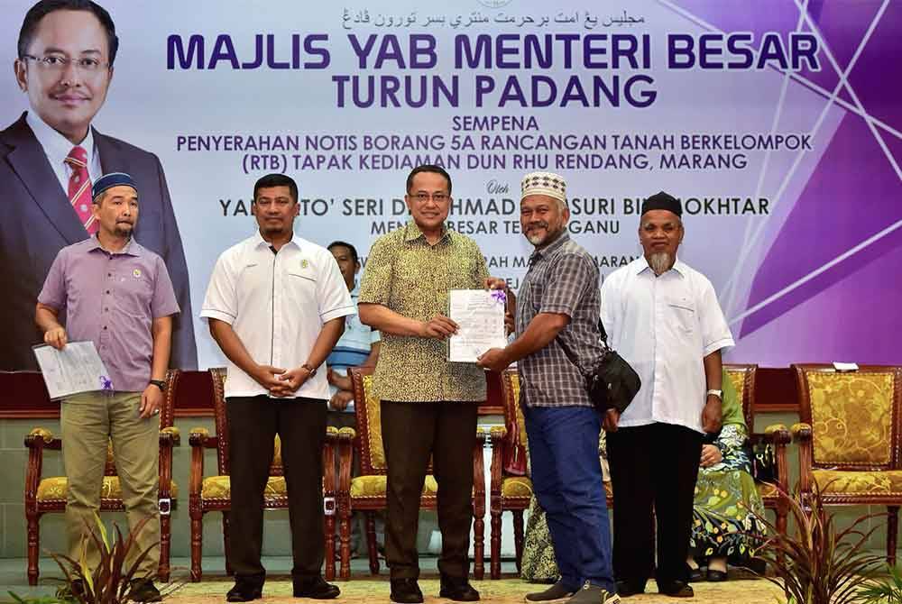 Ahmad Samsuri (tengah) menyerahkan geran hak milik 5A kepada seorang penerima pada majlis diadakan di Dewan Utama, Majlis Daerah Marang.
